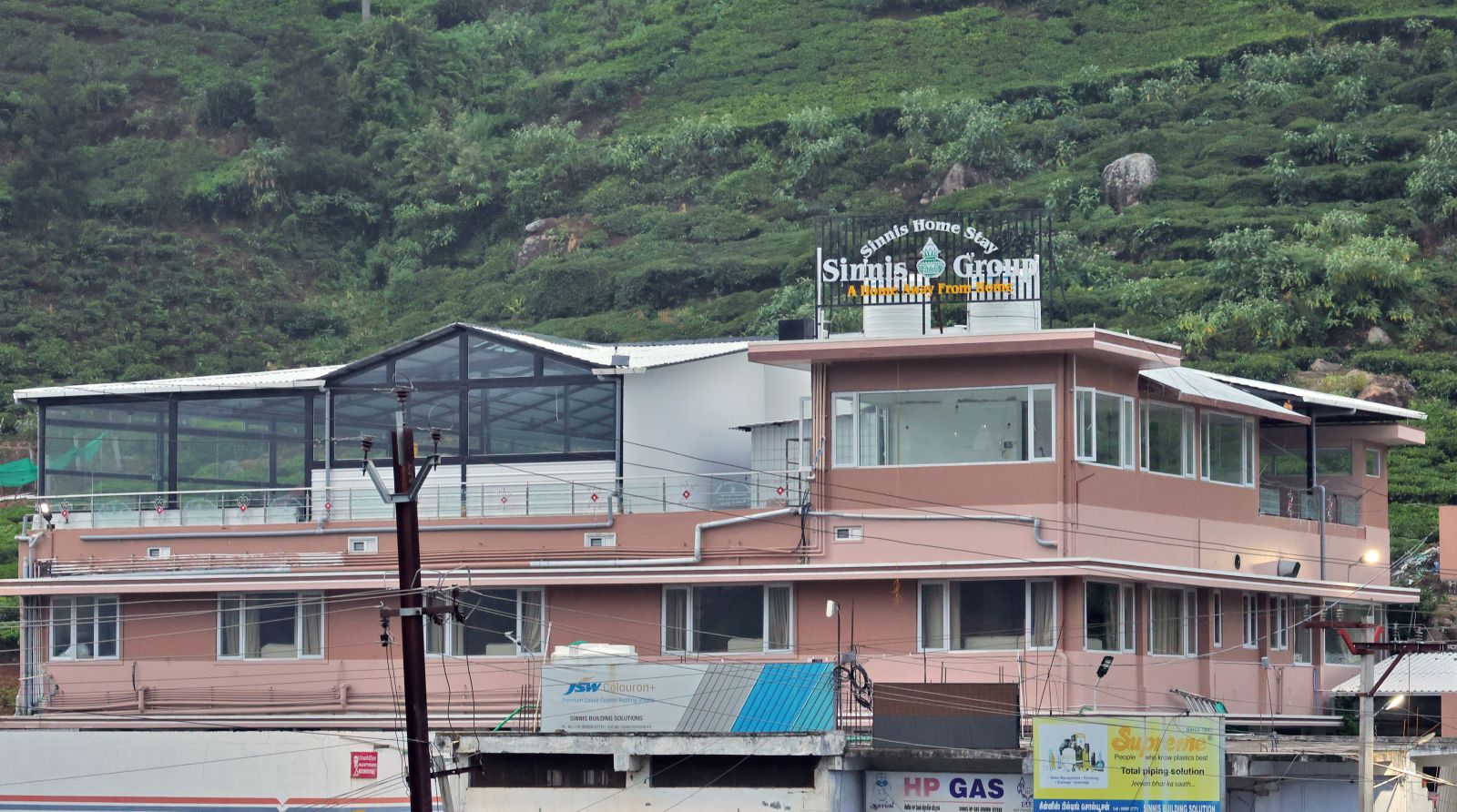 Sinnis Home Stay building set against a tea-covered hillside in Kattabettu